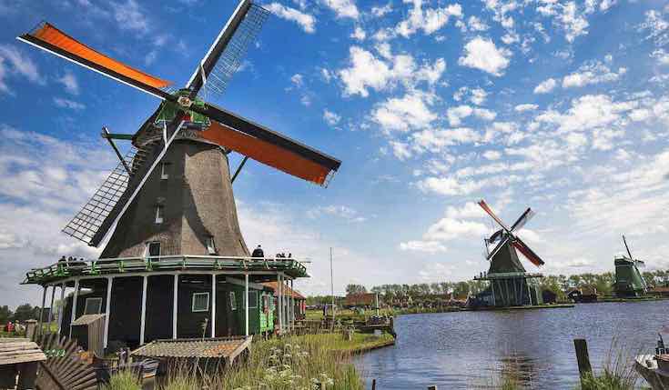 three dutch windmills on a sunny day next to a water canal
