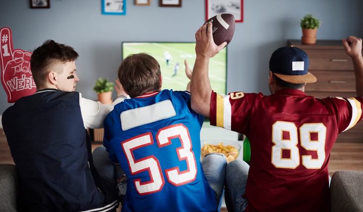 Three men in football t-shirts are watching TV
