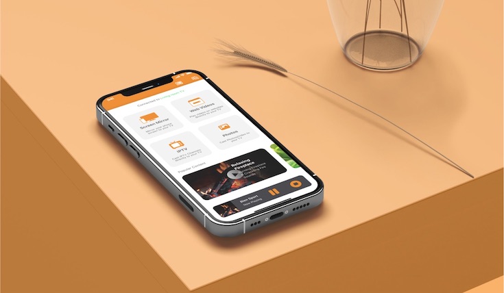 An iPhone laying on an orange surface. There is a wheatear and a round metallic object next to the iPhone. The iPhone has the AirBeamTV Mirror For Fire TV app on the screen