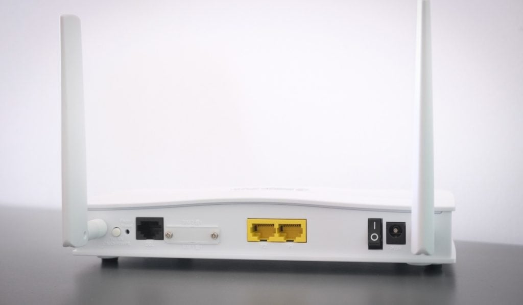 A pale router rests on a contrasting dark surface. Its WLAN ports shine in vibrant yellow, while the power plugs remain sleek in black.