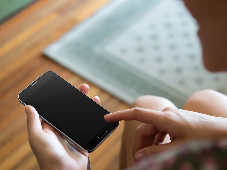A person tapping the screen of an Android smartphone. The smartphone has a black screen